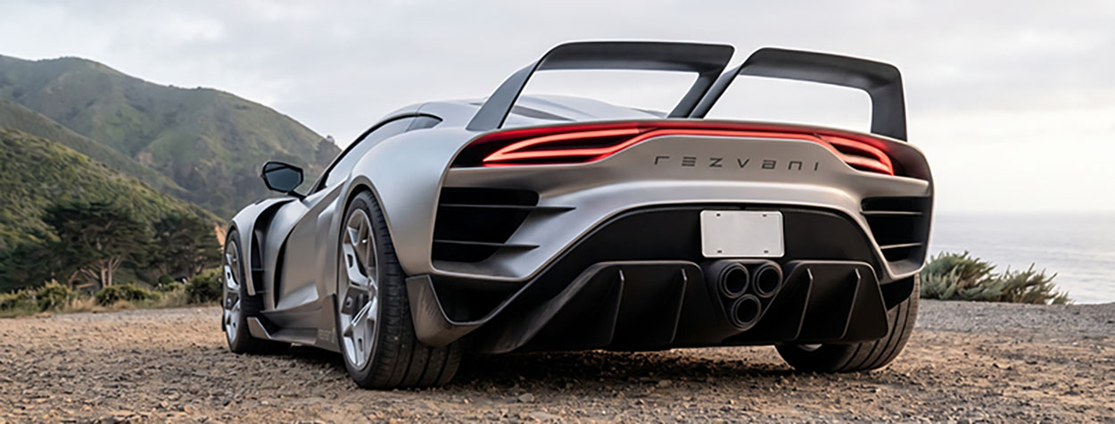 Vue arrière d'une hypercar Rezvani Beast X gris argenté avec son grand aileron, sur une route de côte en terre.