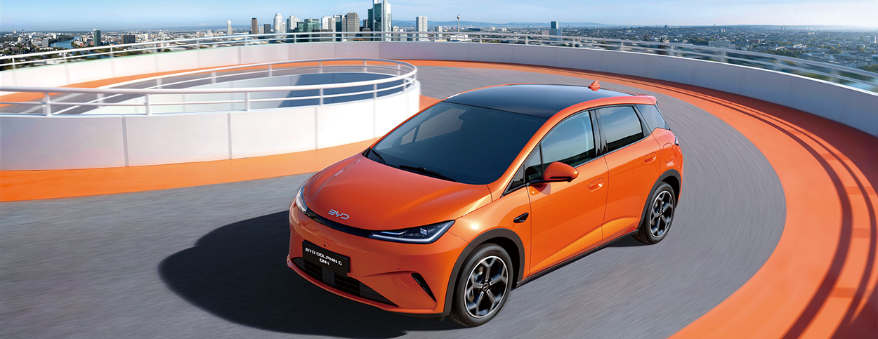 Citadine BYD DOLPHIN G DM-i de couleur orange avec toit noir, roulant sur une rampe circulaire en hauteur avec une vue panoramique sur une grande ville moderne en arrière-plan.