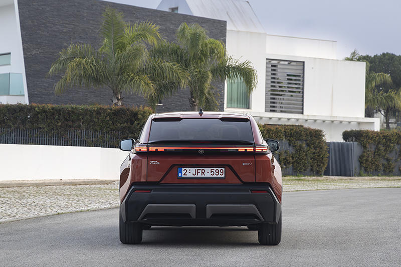 Vue arrière statique du Toyota C-HR+ 2026 électrique, coloris Metal Oxide, soulignant le bandeau lumineux LED012