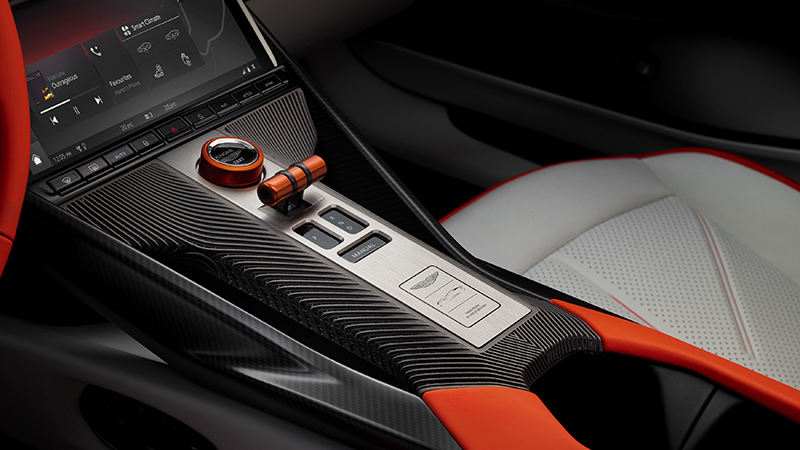 Console centrale d'une Aston Martin Valen avec bouton Start orange, sélecteur de vitesse, finition carbone et écran d'infodivertissement