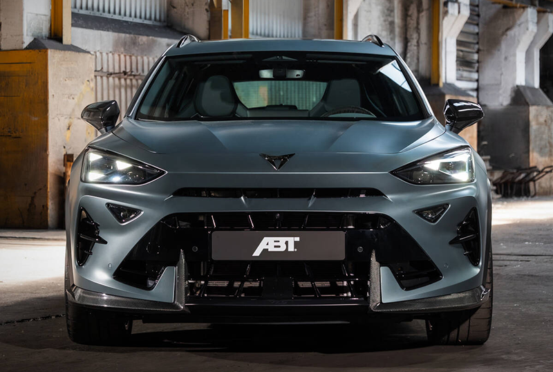 Vue frontale de face d'un CUPRA Formentor VZ5 de couleur gris satiné mat, stationné dans un atelier industriel en béton et métal.