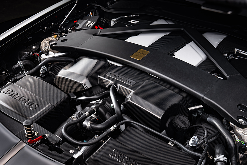 Vue rapprochée du moteur V12 biturbo de 5,2 litres de la BRABUS BODO, avec ses caches en fibre de carbone, sa barre anti-rapprochement noire et le logo BRABUS gravé.