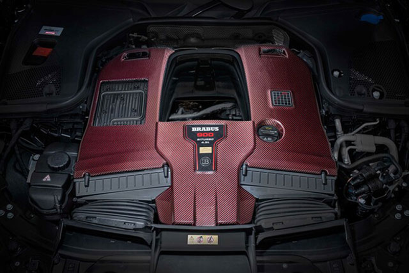 Gros plan sur le moteur V8 biturbo Brabus avec son cache en fibre de carbone rouge et noir et le badge gravé du préparateur de Bottrop. Détail mécanique haute performance.