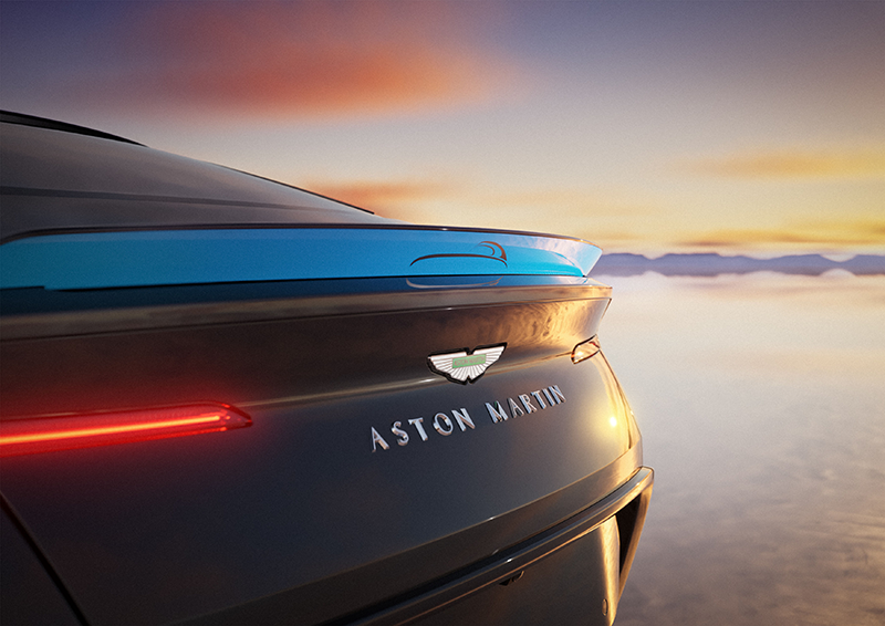Gros plan sur l'arrière d'une Aston Martin DB12 S noire avec aileron bleu au coucher du soleil.