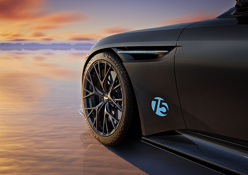 Gros plan sur l'aile avant et la roue d'une Aston Martin DB12 S noire avec le badge "75" bleu, sur un lac salé au coucher du soleil.