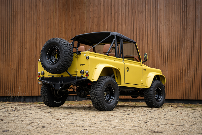 Vue arrière 3/4 Land Rover Defender 90 MIYO Nomad jaune, pneus tout-terrain, arceau de sécurité et toit bikini